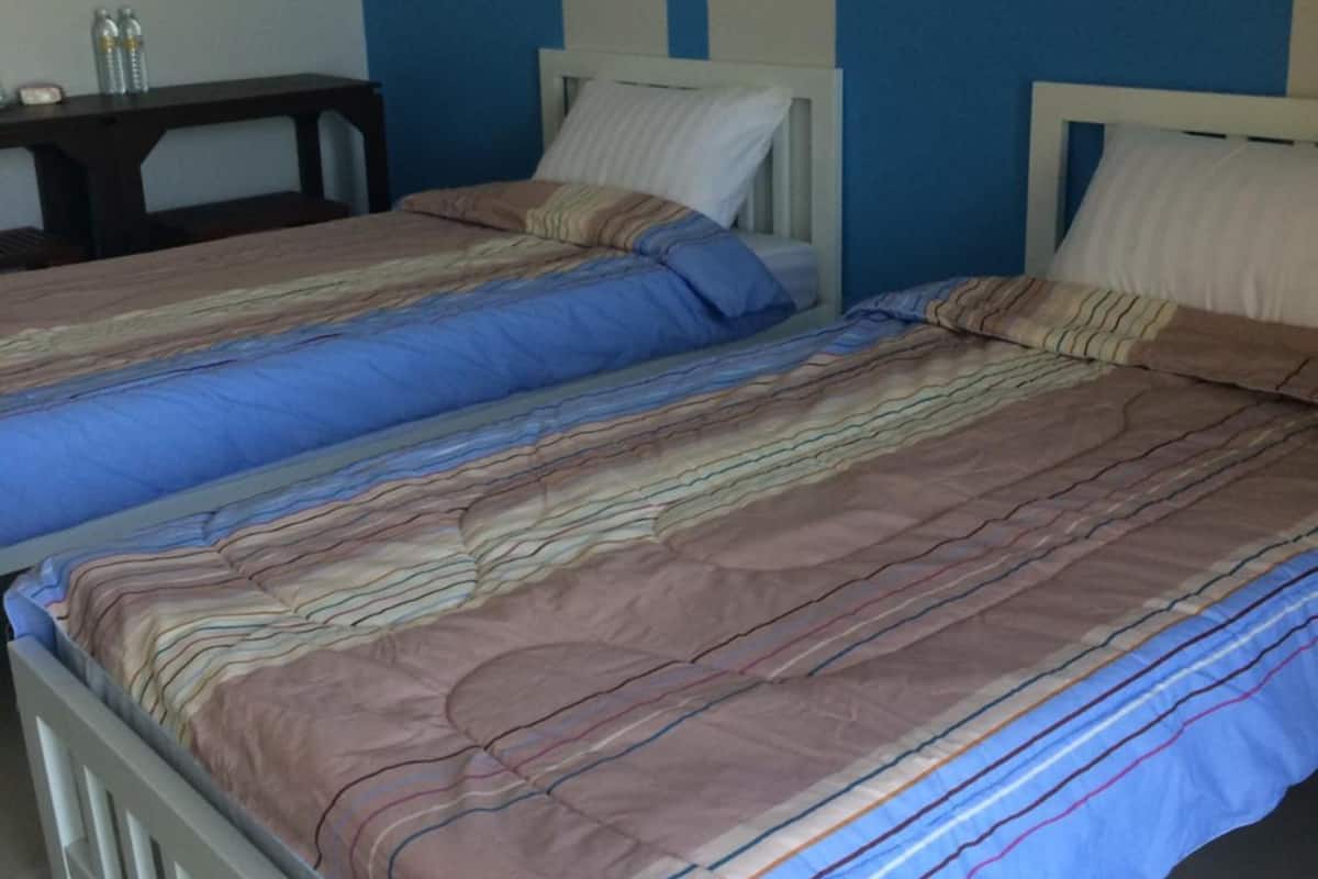 A room with two beds, each with a striped bedspread and white pillows. There is a small table with two bottles on it. The walls are painted blue and white.