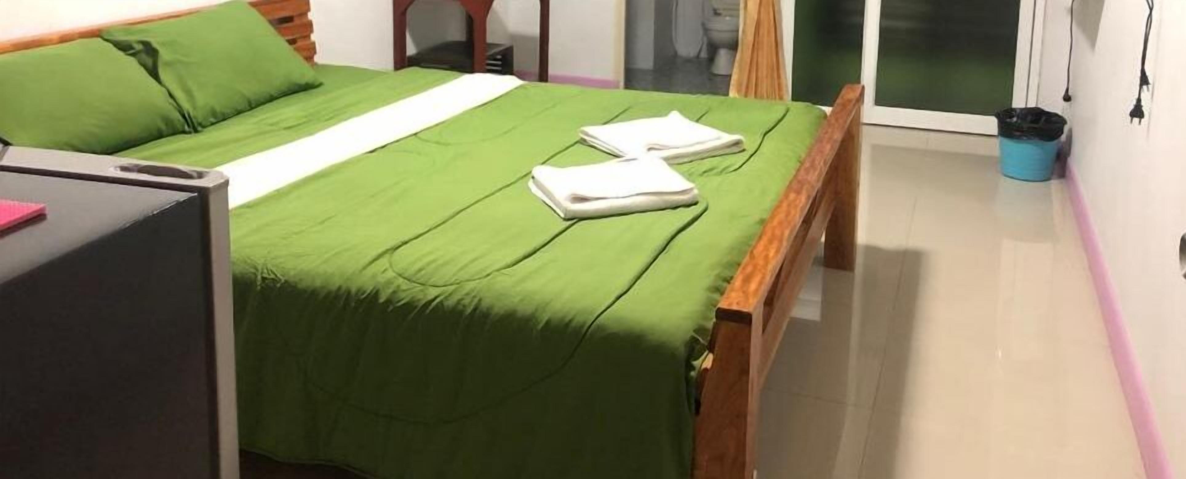 A neatly made bed with a green bedspread and two folded white towels.