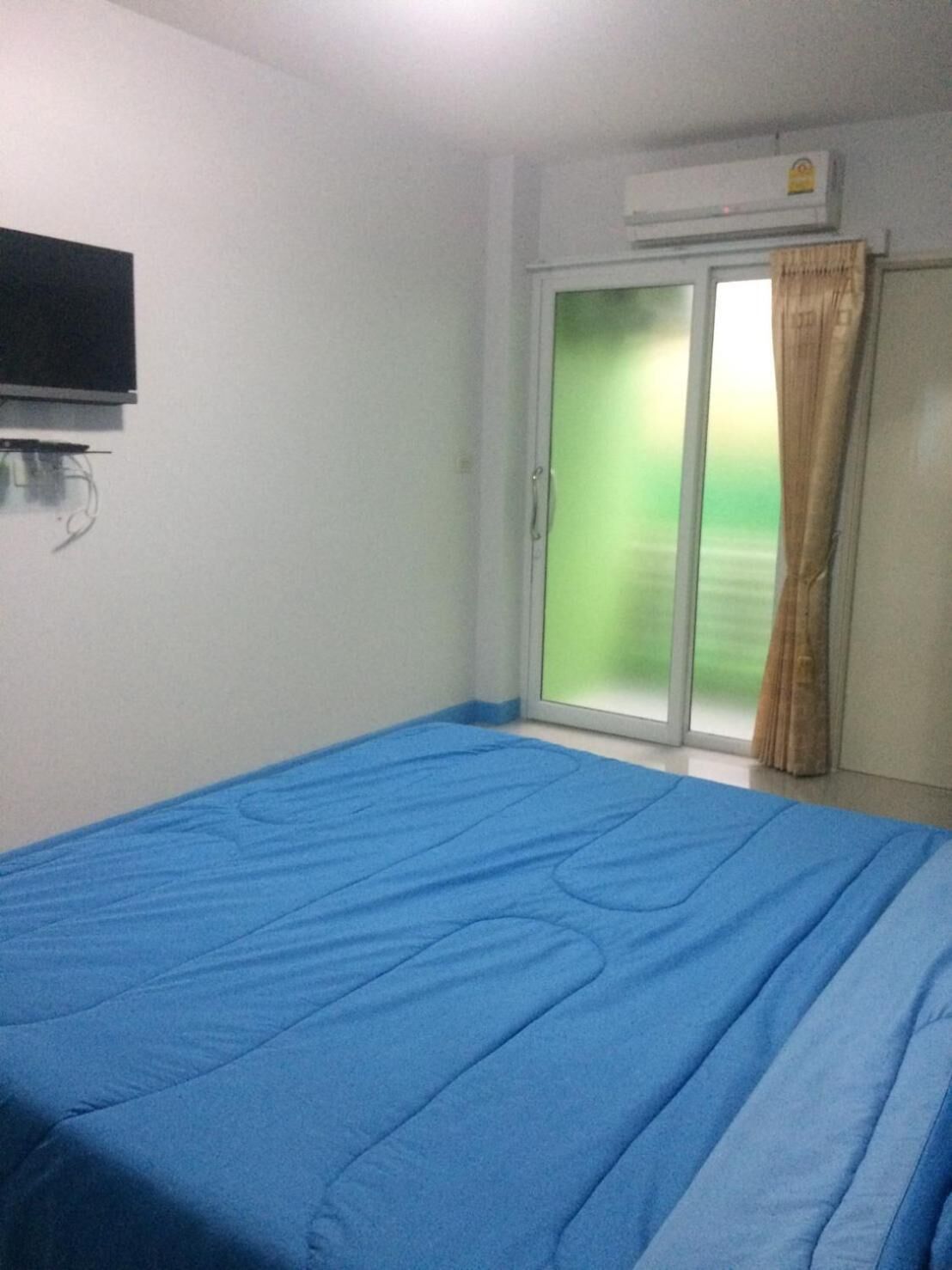 A room with a bed, a television mounted on the wall, and a sliding glass door leading to a balcony.