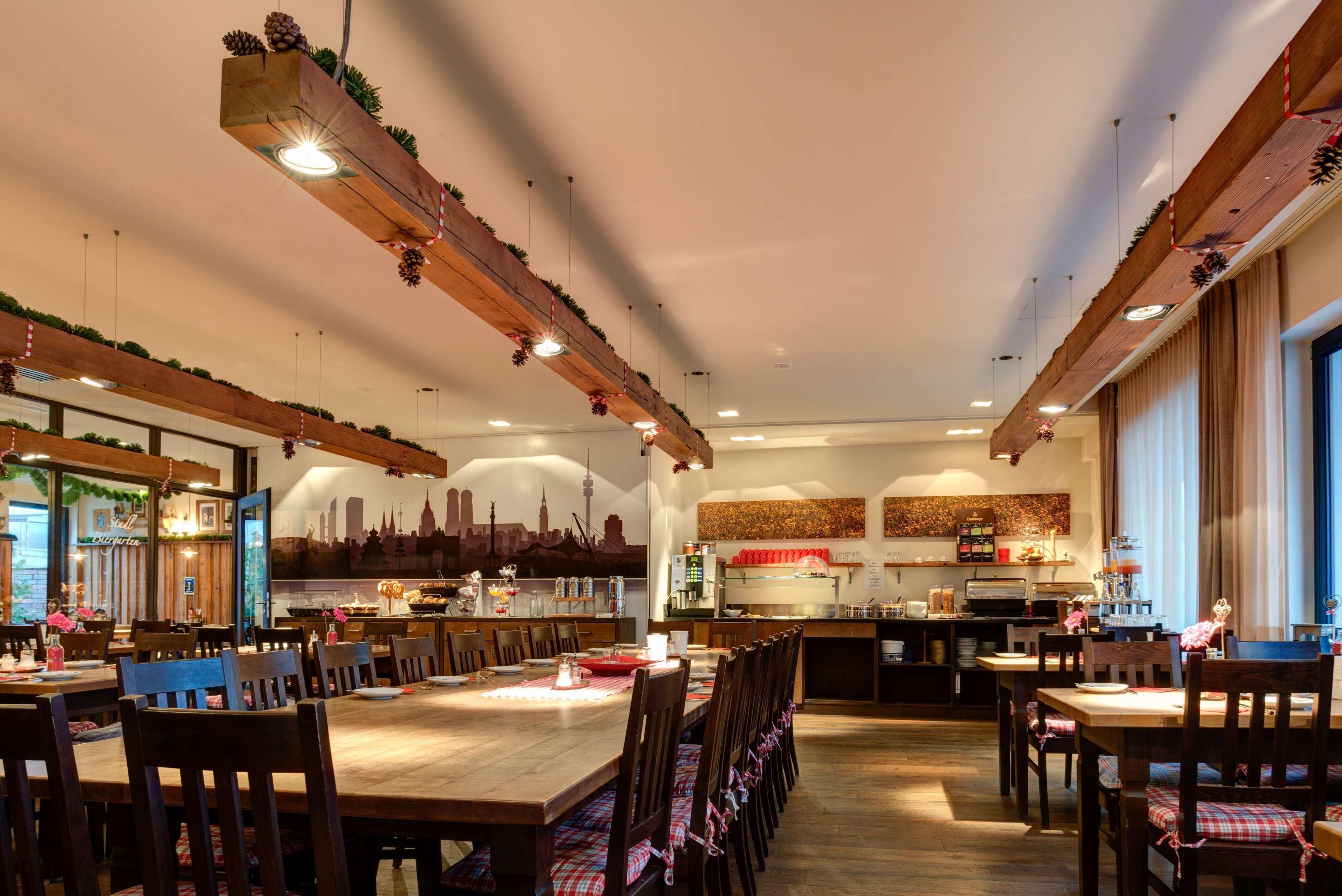 Un restaurant avec des tables et des chaises en bois, une cuisine à l’arrière-plan et une fresque représentant un paysage urbain sur le mur.