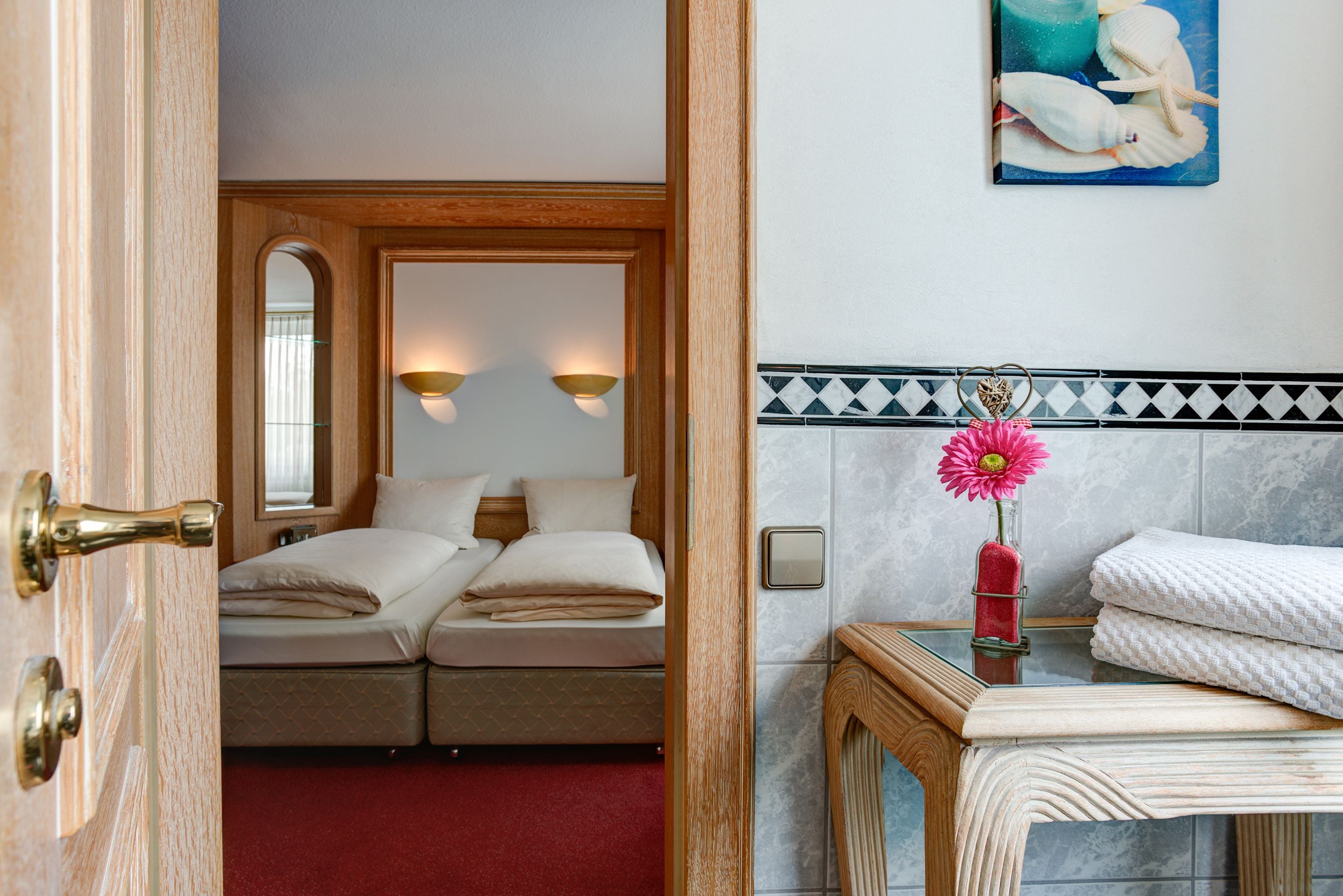 Habitación de hotel con cama doble, baño pequeño con espejo y un cuadro en la pared.