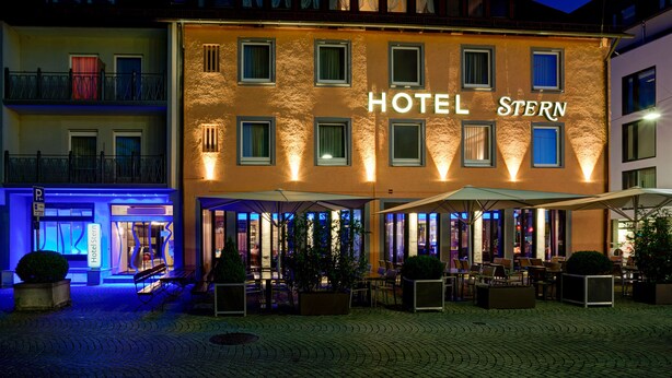 Un hotel con un letrero que dice "HOTEL STERN" y asientos al aire libre con sombrillas.