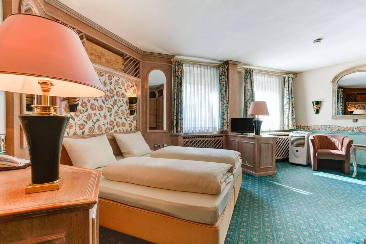 Una habitación de hotel con cama, escritorio, silla, televisión y espejo.