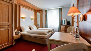 Una habitación de hotel con dos camas, un escritorio, una silla, una lámpara, un televisor y un minibar.