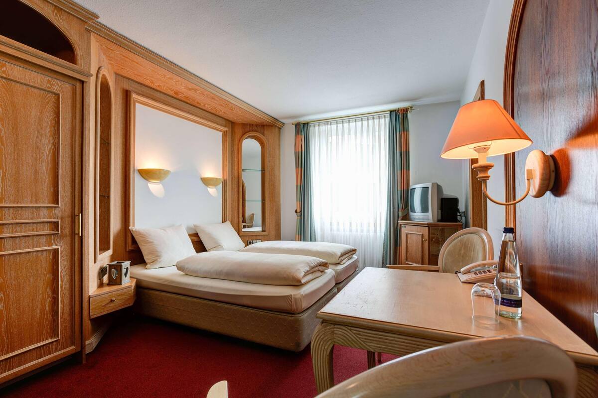 Una habitación de hotel con dos camas, un escritorio, una silla, una lámpara, un televisor y un minibar.