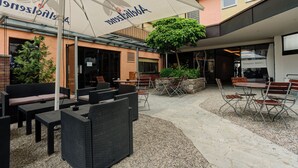 Un área de estar al aire libre con mobiliario de mimbre, un paraguas grande y un edificio con un letrero.