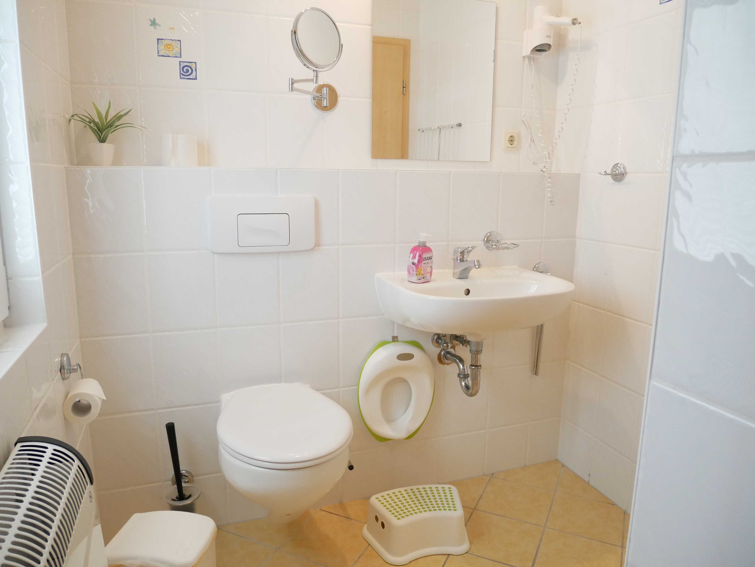 Een badkamer met toilet, bidet, wastafel, spiegel en een kleine potplant.