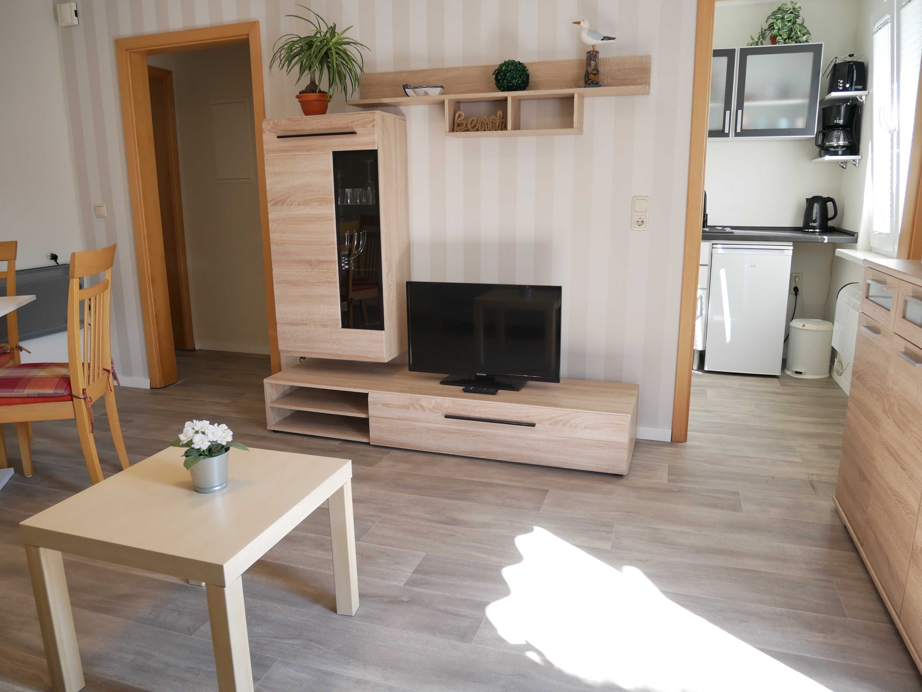 En moderne stue med TV, træmøbler, et spisebord og et køkken med hårde hvidevarer.