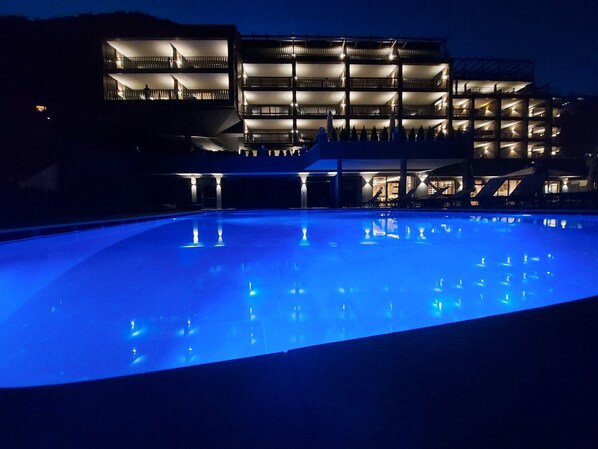 Un bâtiment moderne doté de nombreux balcons et d’une piscine illuminée la nuit.