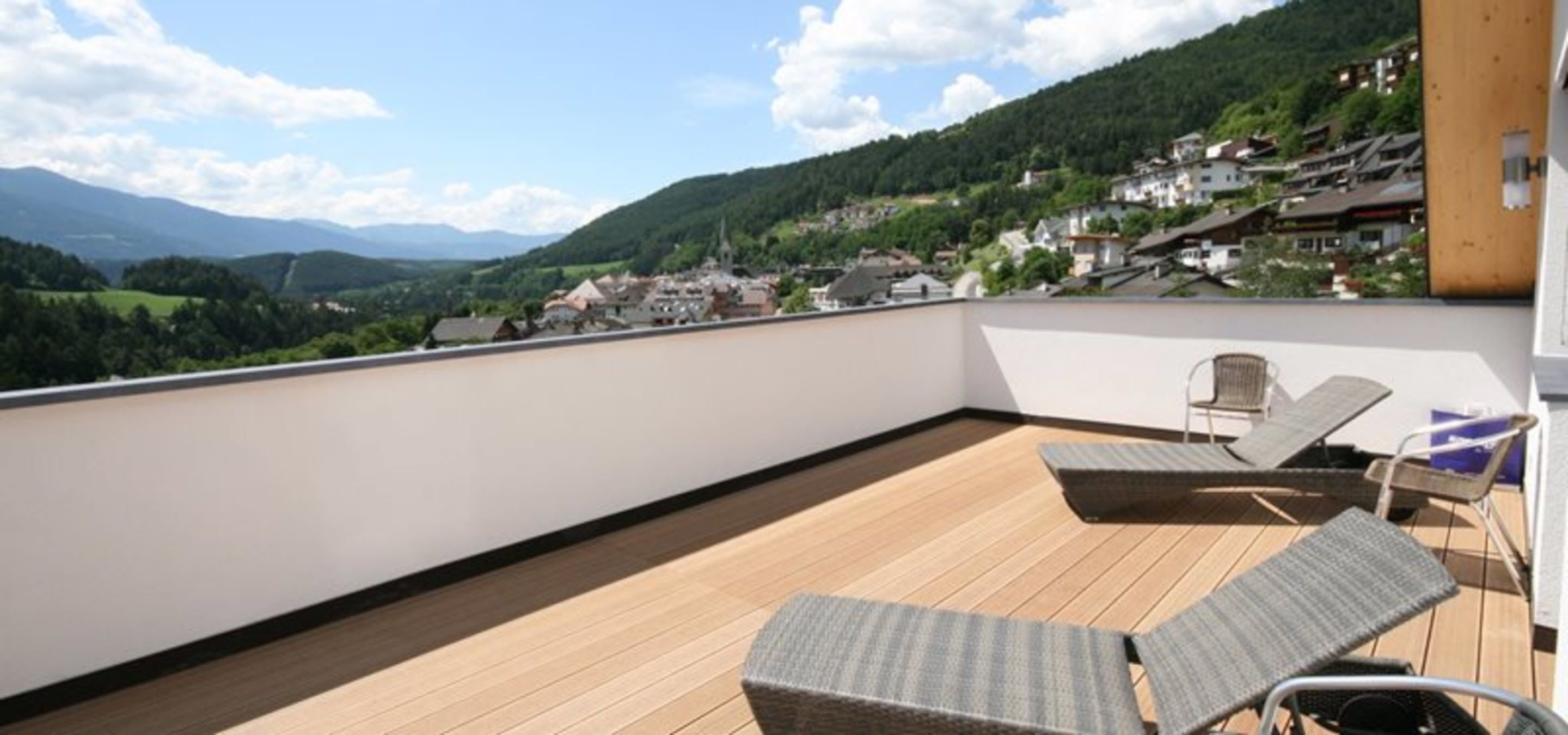 Een balkon met twee loungesteunen en uitzicht op een dorp en bergen.