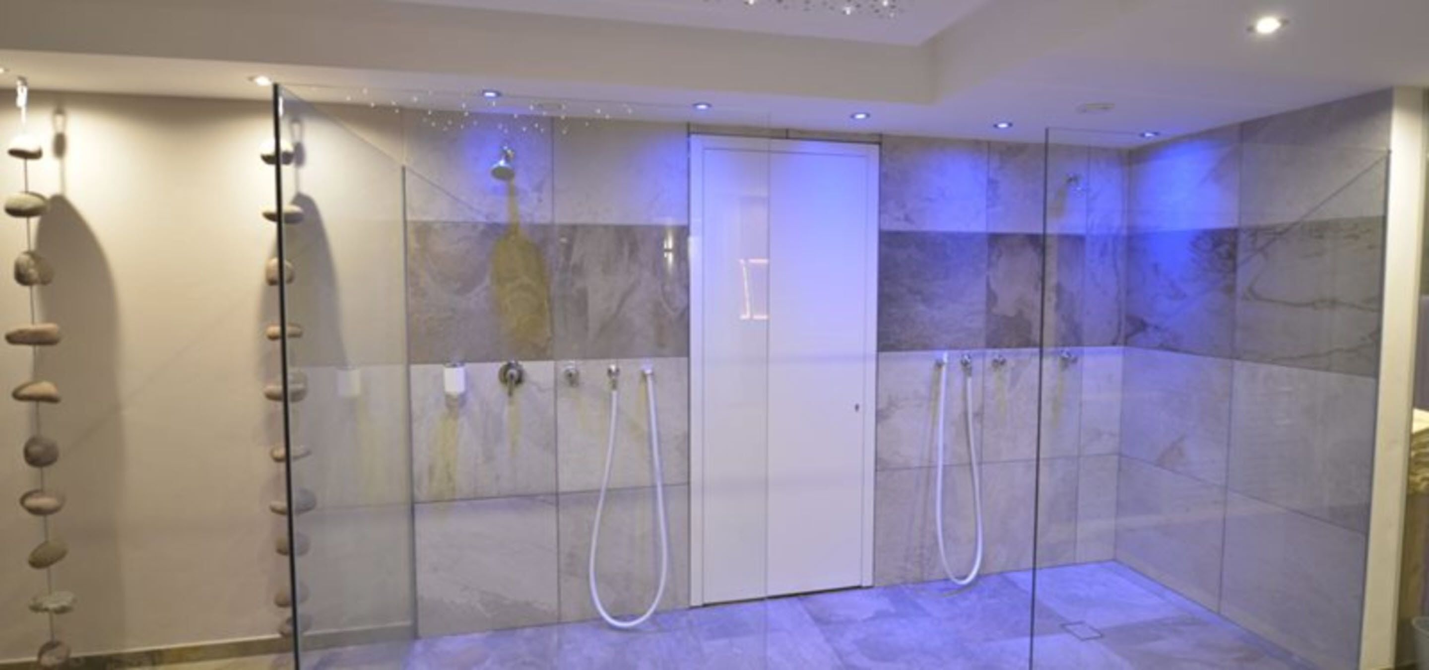 A modern bathroom with a glass-enclosed shower, marble tiles, and a stone wall decoration.