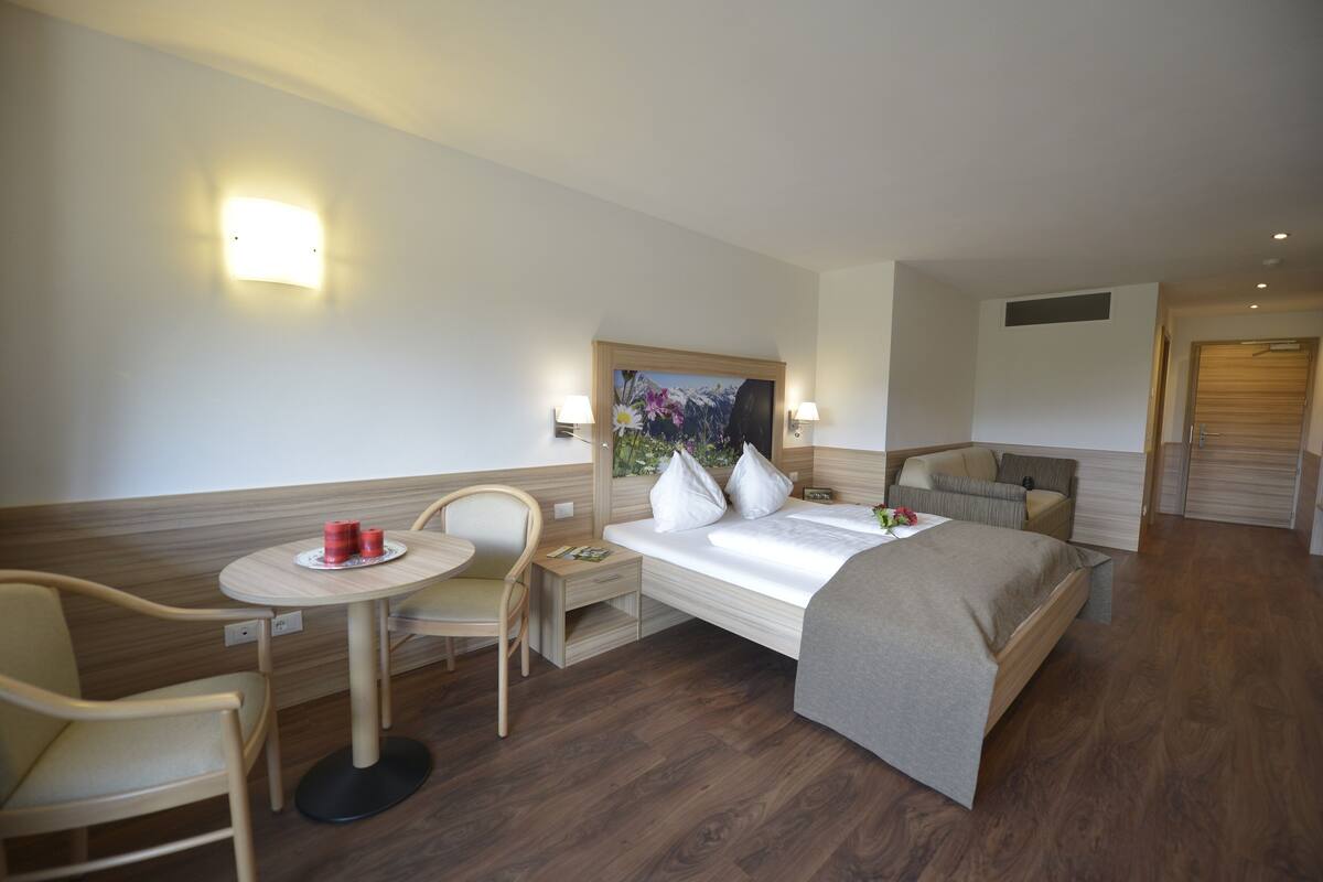 Une chambre d’hôtel avec un lit, une petite table et deux chaises, une table de chevet et un tableau au mur.
