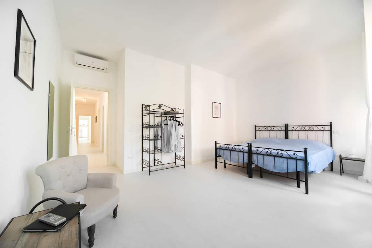 Un dormitorio con cama, una silla, un escritorio y un perchero.