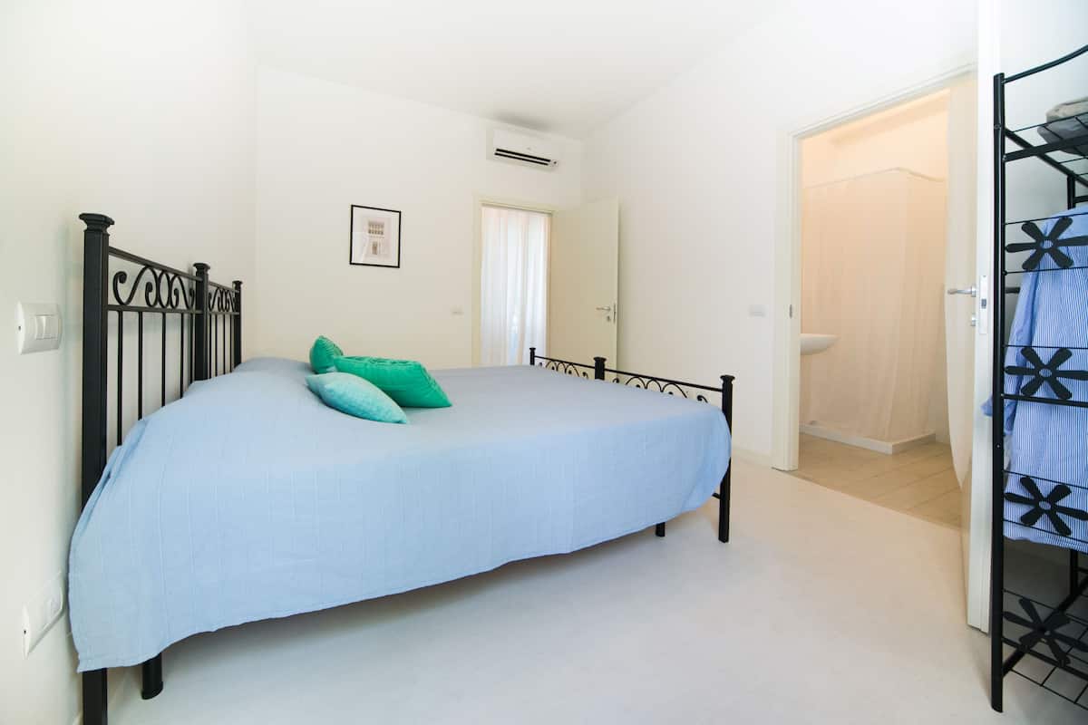 Un dormitorio con cama, puerta y baño a la vista a través de otra puerta abierta.