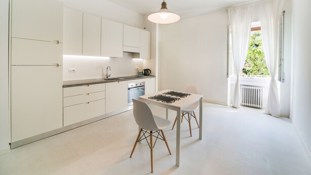 A modern kitchen with white cabinets, a dining table with chairs, and a pendant light. - Casa Italia (Verona)