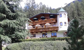 A multi-story hotel with balconies, a tower, and a mountain backdrop. - Tower room - Haus Waldheim (Oetz)