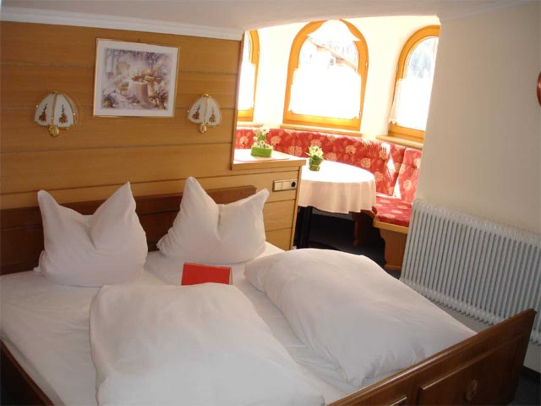 A hotel room with a bed, a small table, a bench, and a radiator.