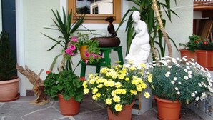 A potted plant arrangement outside a building with a window, a statue, and a green stool. - Tower room - Haus Waldheim (Oetz)