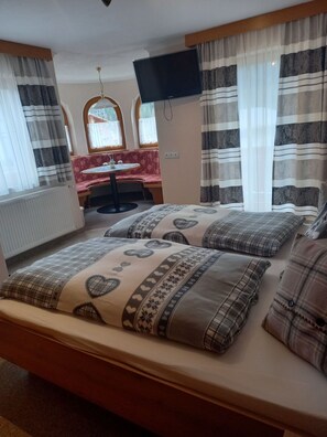 Une chambre à coucher avec un lit, une télévision, une fenêtre avec des rideaux et une petite table avec une chaise.