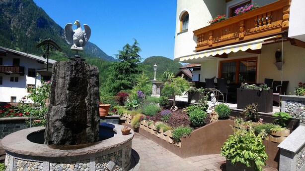 A courtyard with a rock fountain, a statue, and a building with a balcony. - Tower room - Haus Waldheim (Oetz)
