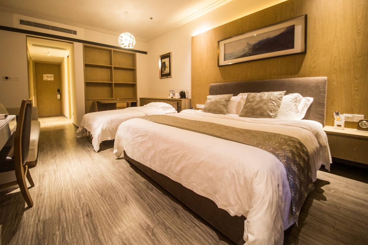 Ein Hotelzimmer mit zwei Betten, einem Schreibtisch und einem Stuhl. Es gibt ein hölzernes Kopfstück, ein gerahmtes Bild an der Wand und ein Holzregal.