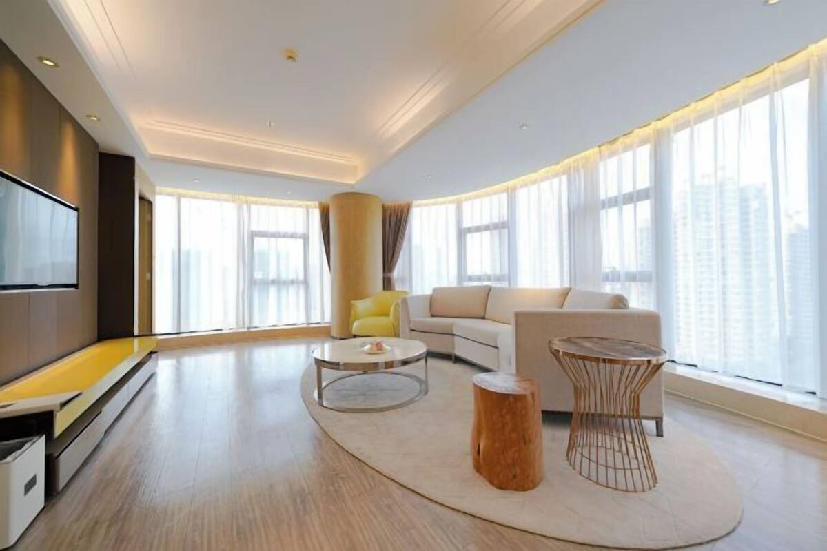 Ein modernes Wohnzimmer mit einer Couch, zwei Couchtischen, einem Fernseher und großen Fenstern.