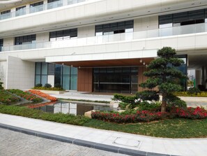 A modern building with a glass entrance, a landscaped garden with shrubs and flowers, and a small water feature. - Dahengqin Superior Talent Hotel (Hengqin Port Branch) (Zhuhai)