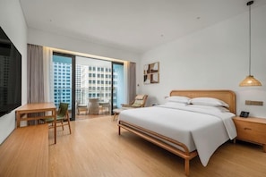 A modern hotel room with a large bed, a desk, and a chair. There is a view of a cityscape through the window. - Dahengqin Superior Talent Hotel (Hengqin Port Branch) (Zhuhai)
