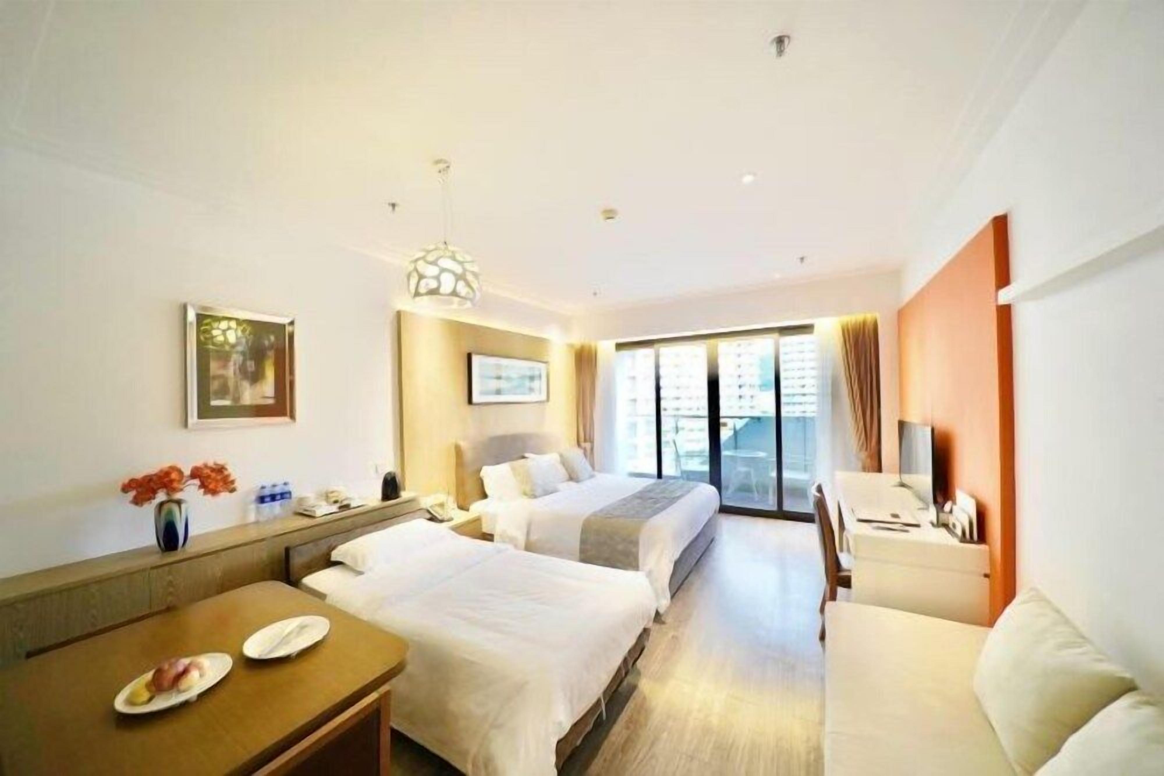 A hotel room with two beds, a desk, a chair, a dining table, and a large window.