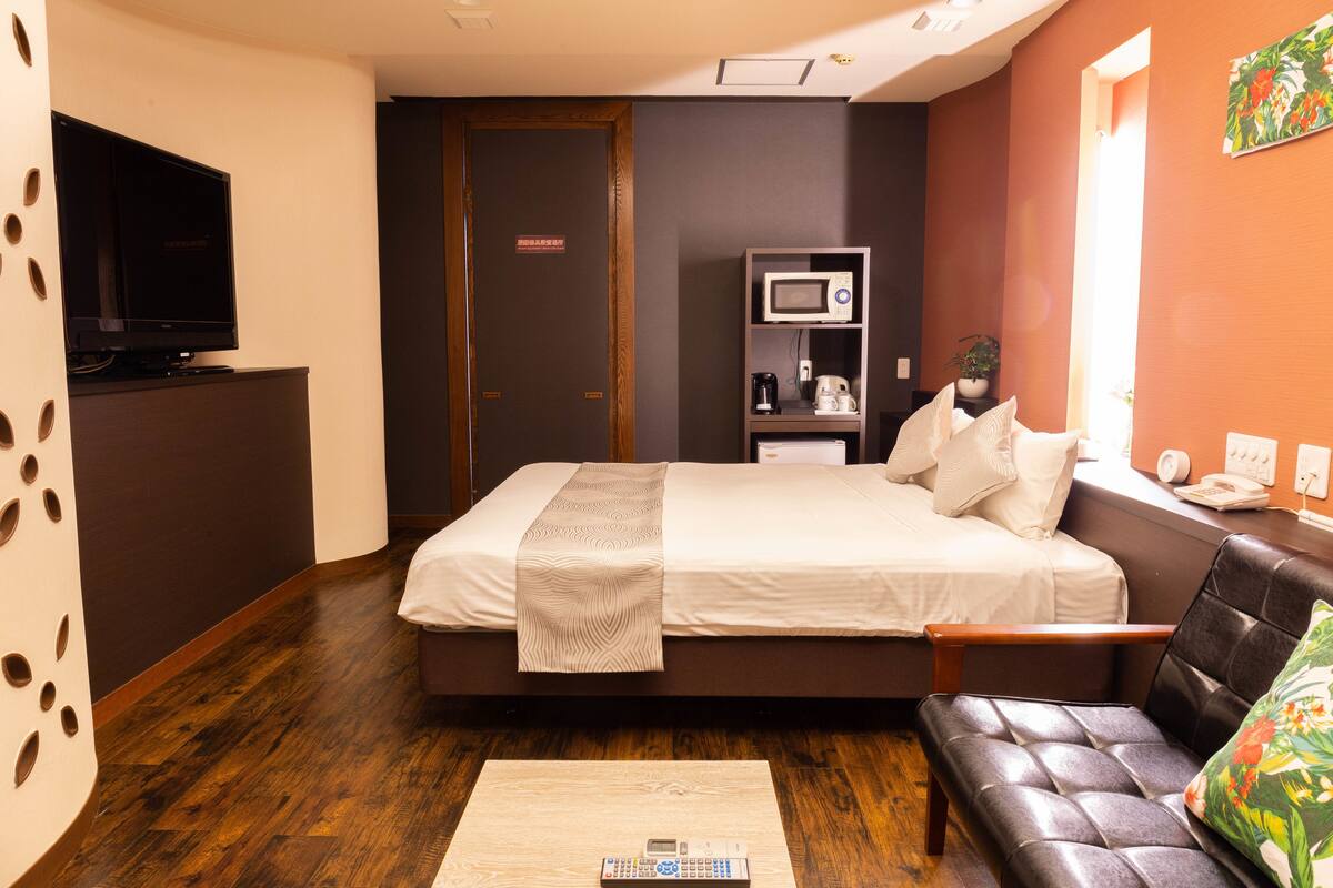 A hotel room with a bed, a sofa, a television, a microwave, and a coffee maker.