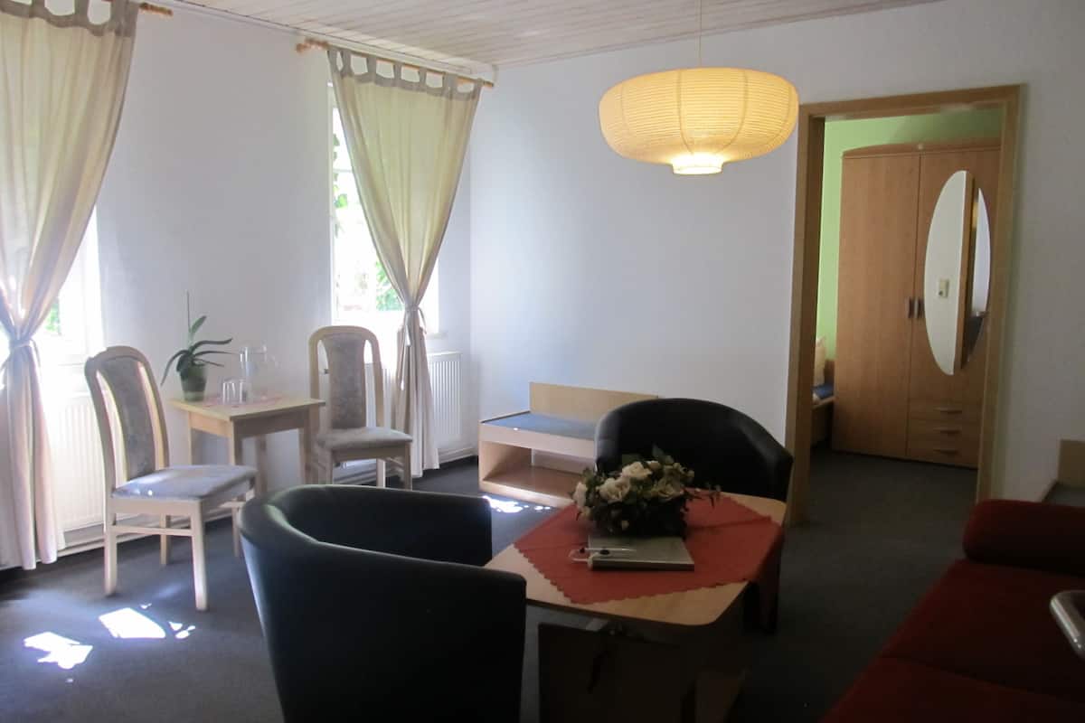 Une pièce comprenant une table à manger, des chaises, un canapé, une petite table avec un vase et un miroir au mur.