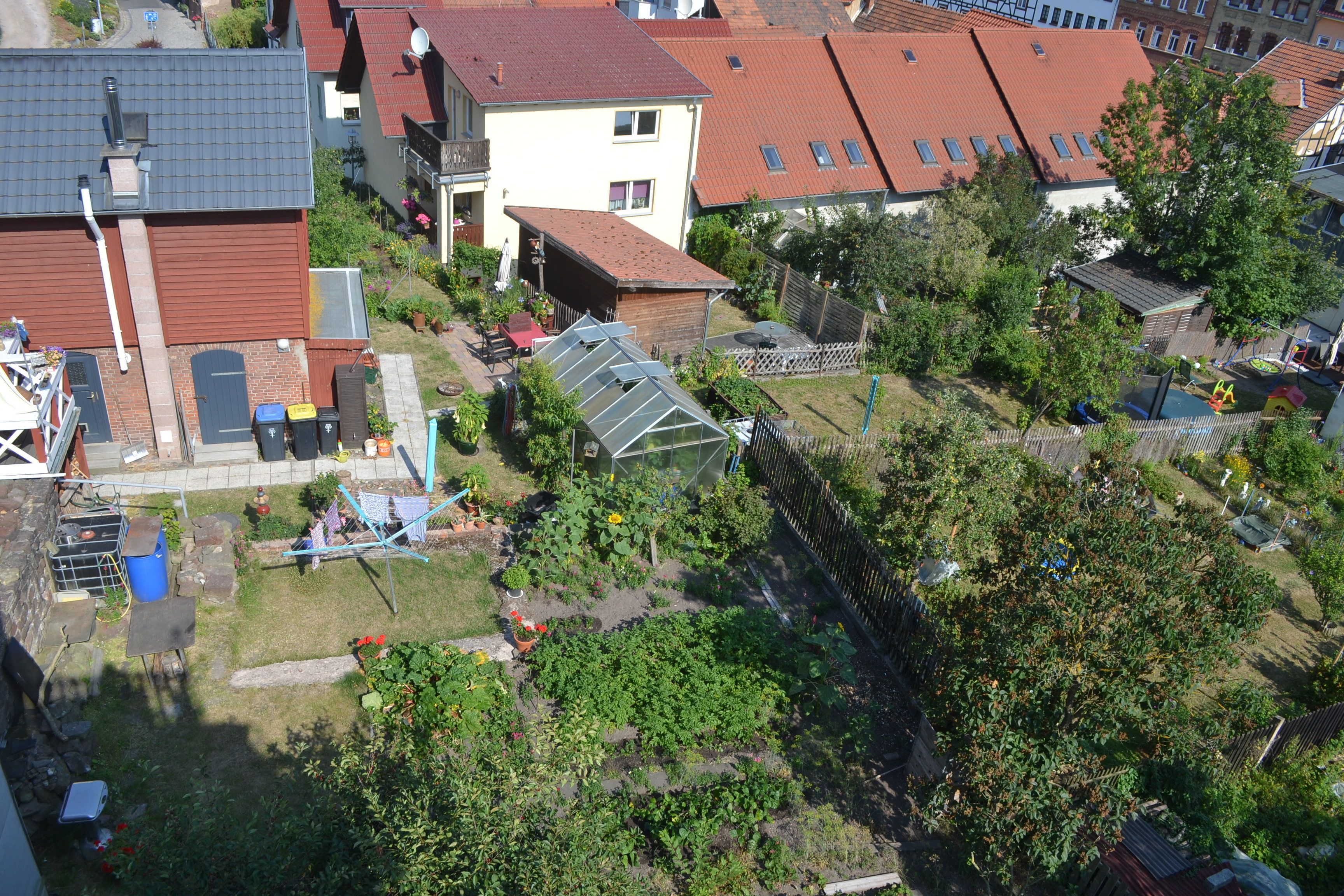 Eine Luftaufnahme eines Wohngebiets mit Häusern, einem Gewächshaus und einem eingezäunten Garten.