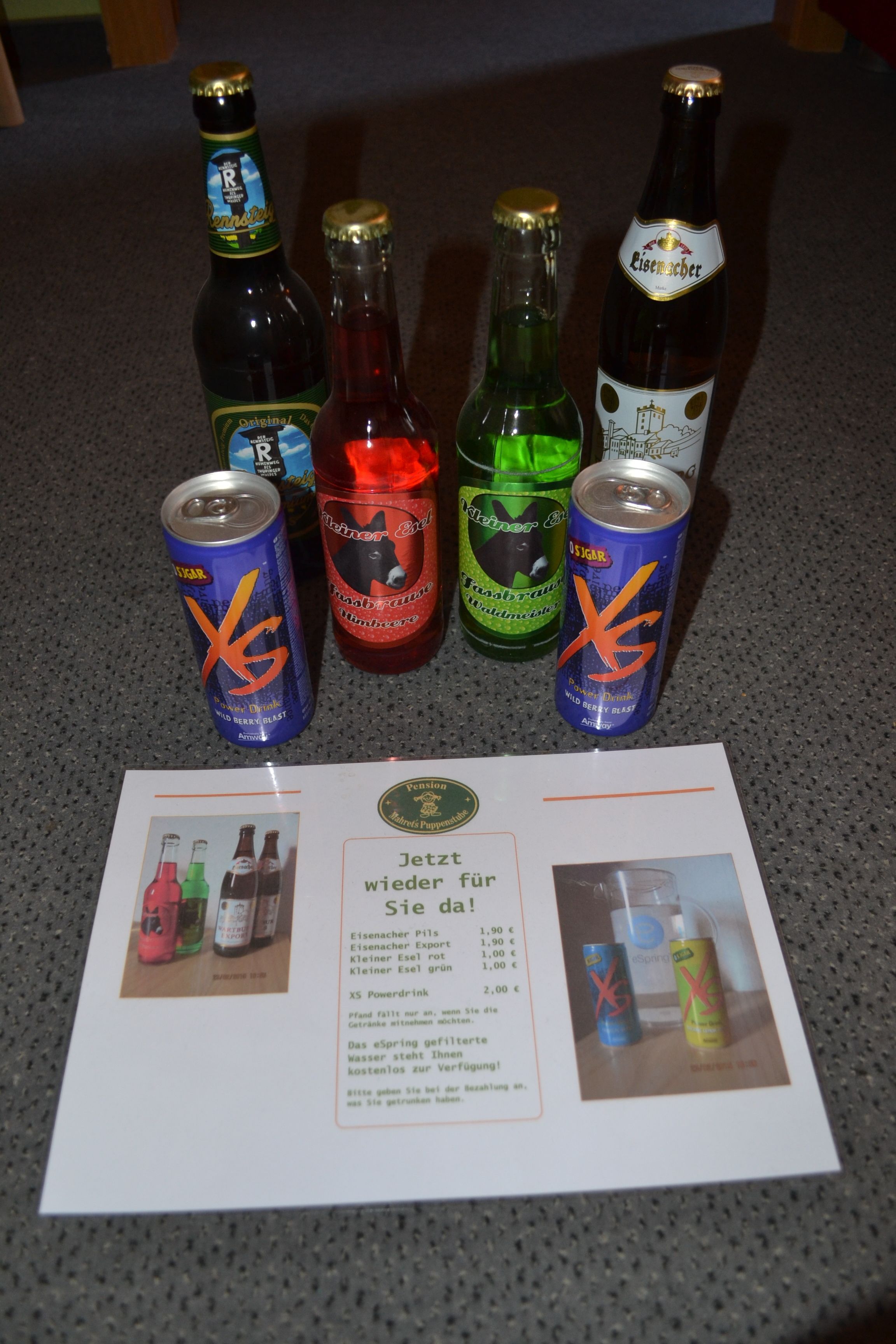 A table with six bottles and two cans of X5 Powerdrink, a menu with prices, and a beverage advertisement.