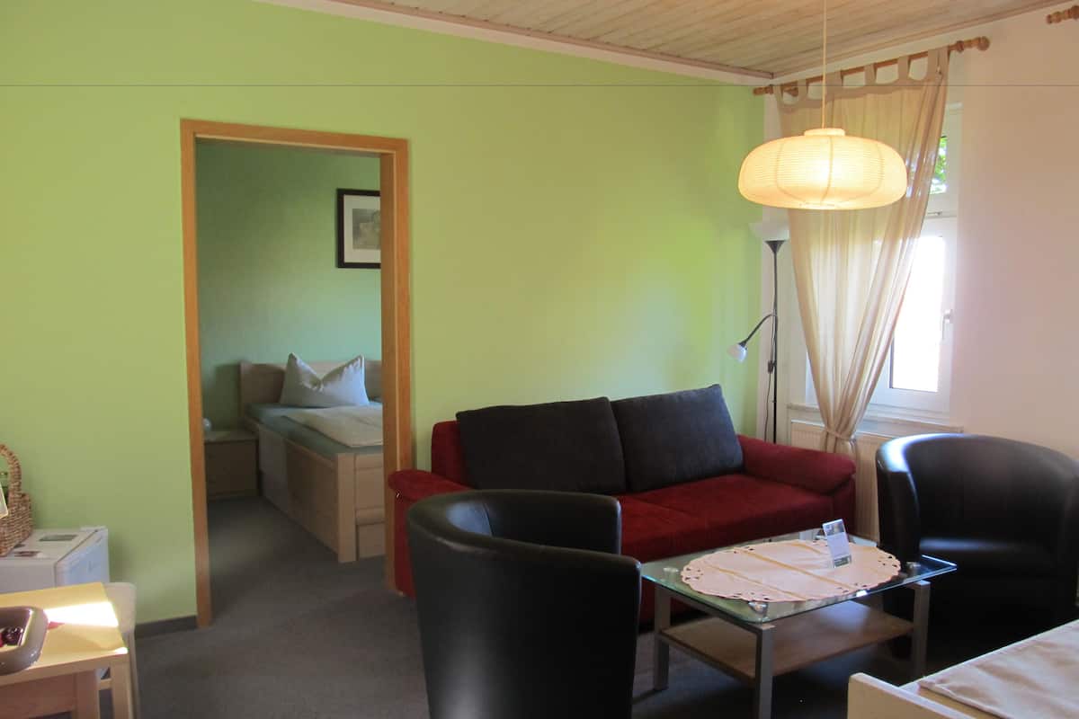 Une pièce avec un canapé rouge, des chaises noires, une table basse en verre et une lampe.