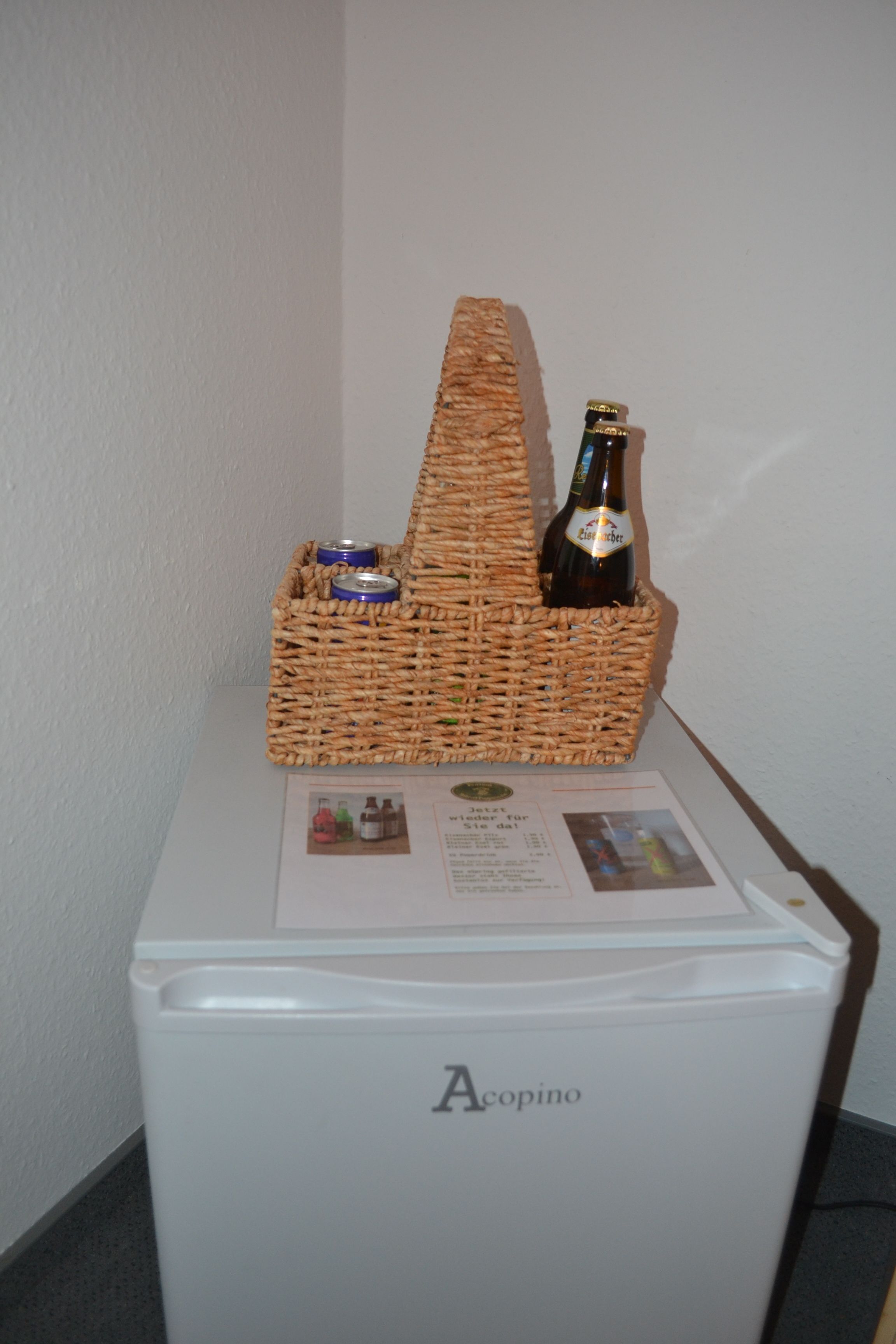 Ein weißer Kühlschrank mit einer Bierflasche und einem Korbwannen-Aufbewahrungsbehälter voller Dosen.
