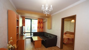 A compact living space with a sofa, a small table, a wooden cabinet, and a bed in the adjacent room. - Tanya Hotel (Sunny Beach)