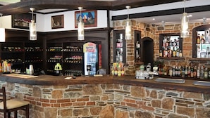 A stone bar with wooden beams, a wine rack, and a variety of liquor bottles. - Tanya Hotel (Sunny Beach)