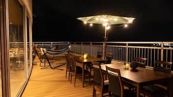 Een terras buiten met een eettafel, stoelen, een hangmat en een parasol.
