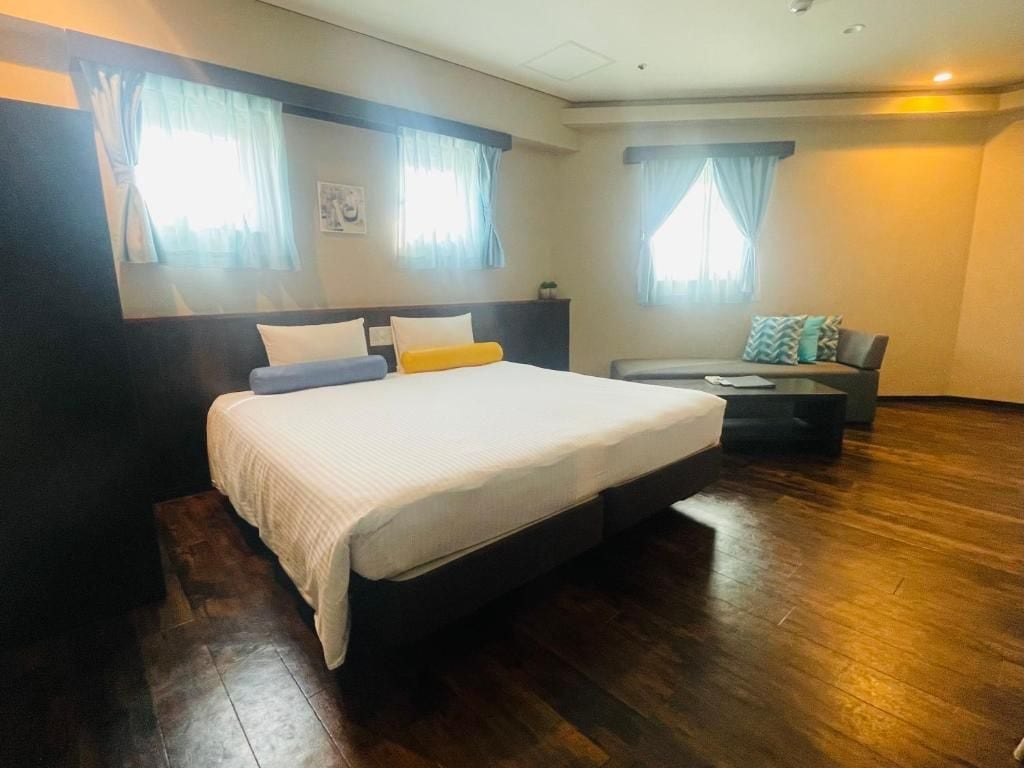A hotel room with a large bed, a sofa, and two windows with curtains.