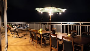 An outdoor deck with a dining table, chairs, a hammock, and a table lamp. - Rycom Crystal Hotel (Okinawa)