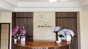 A reception desk with a sign that reads "Bay B&Y Residence" and two flower arrangements. - B&Y Residence (Chiang Mai)