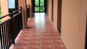 A corridor with red-tiled flooring, a black railing, and a door leading to a green outdoor area. - B&Y Residence (Chiang Mai)