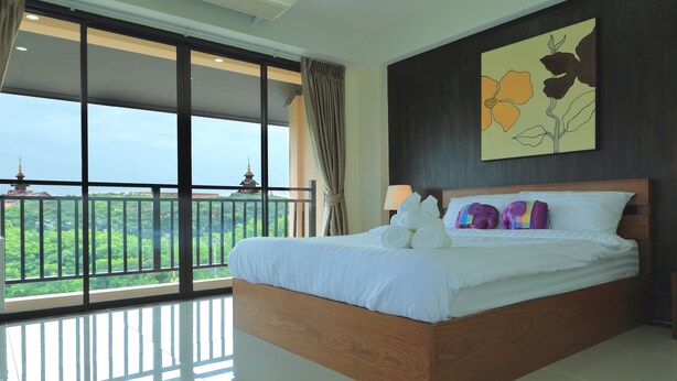 A spacious bedroom with a large bed, a view of greenery and a pagoda through floor-to-ceiling windows, and a wooden headboard. - B&Y Residence (Chiang Mai)