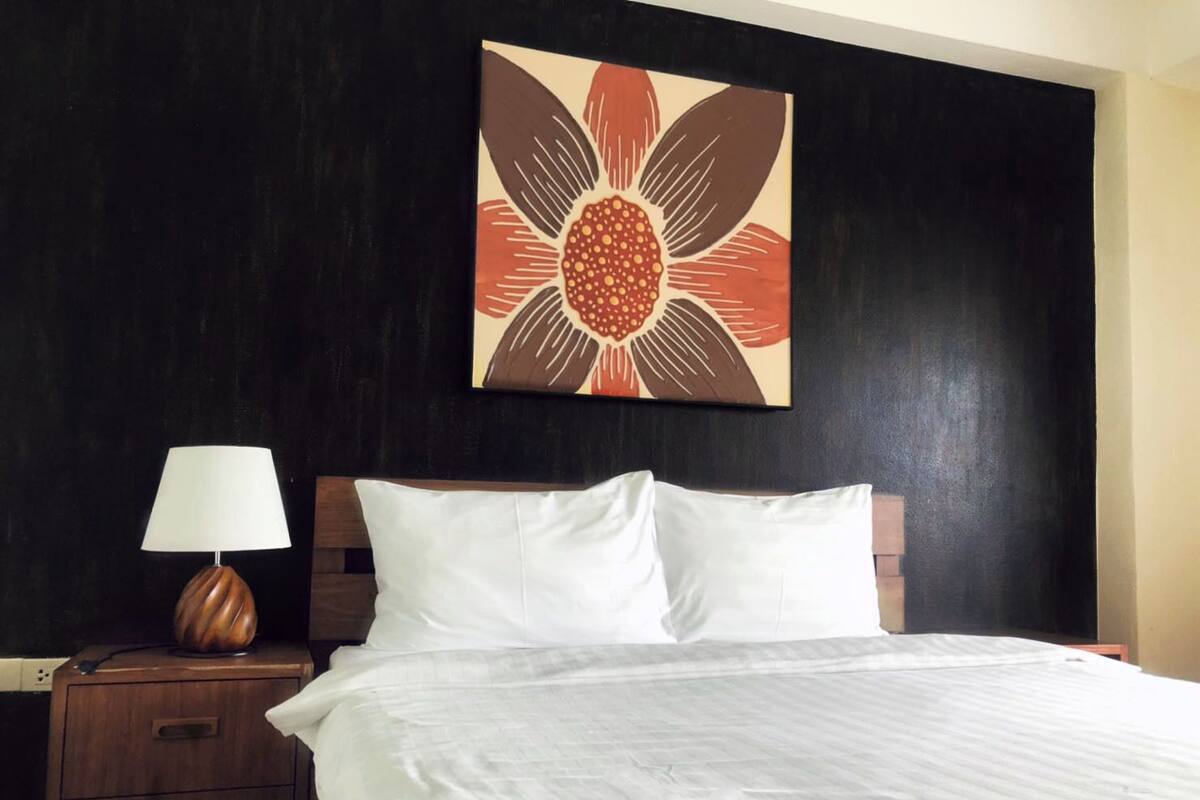 A hotel room with a bed, a nightstand, a lamp, and a wall-mounted artwork.