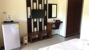 A hotel room with a bed, a desk with a chair, a television mounted on a wall, a wardrobe, and a refrigerator.