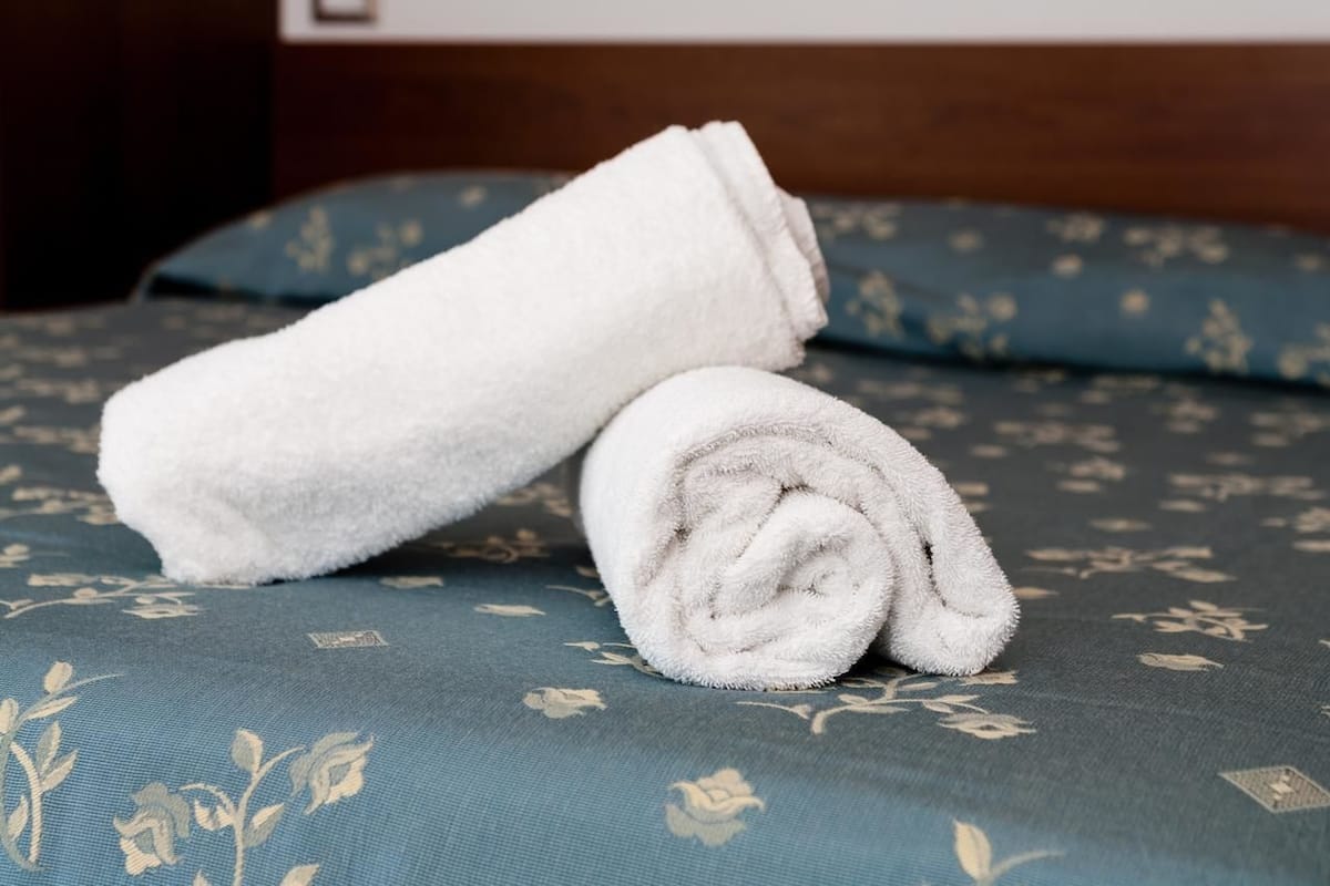 A neatly folded white towel on a bed with a floral-patterned blue bedspread.
