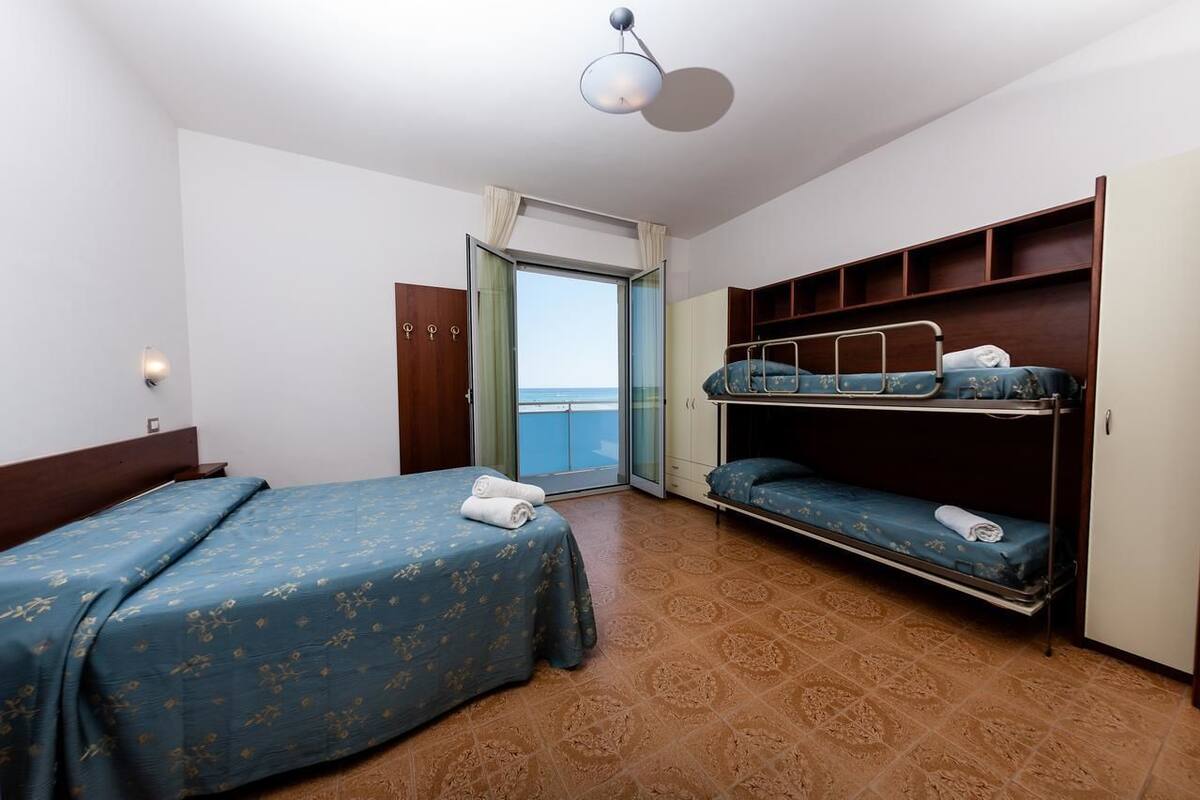 A hotel room with a bed, a bunk bed, a wardrobe, and a view of the sea.