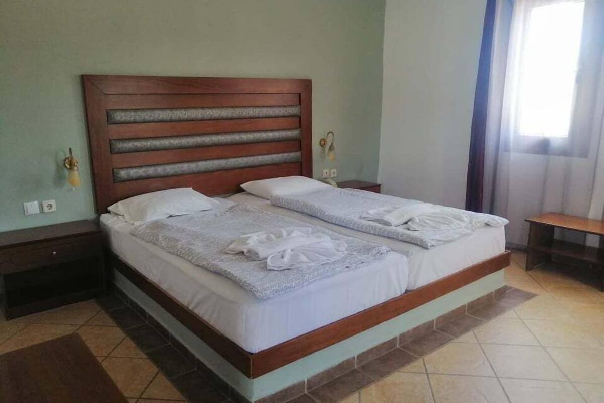 A double bed with a wooden headboard and two pillows, a bedside table, and a nightstand.
