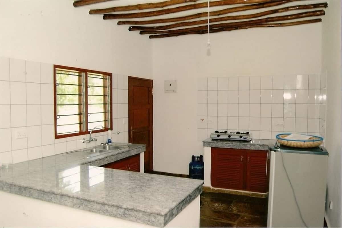 A kitchen with a granite countertop, a gas stove, a refrigerator, and a window with bars.