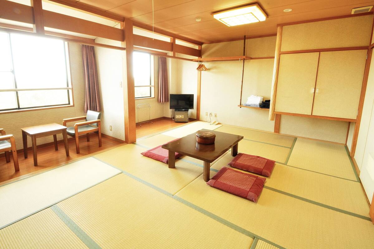 A traditional Japanese-style room with tatami flooring, a low table, cushions, a television, and sliding doors.